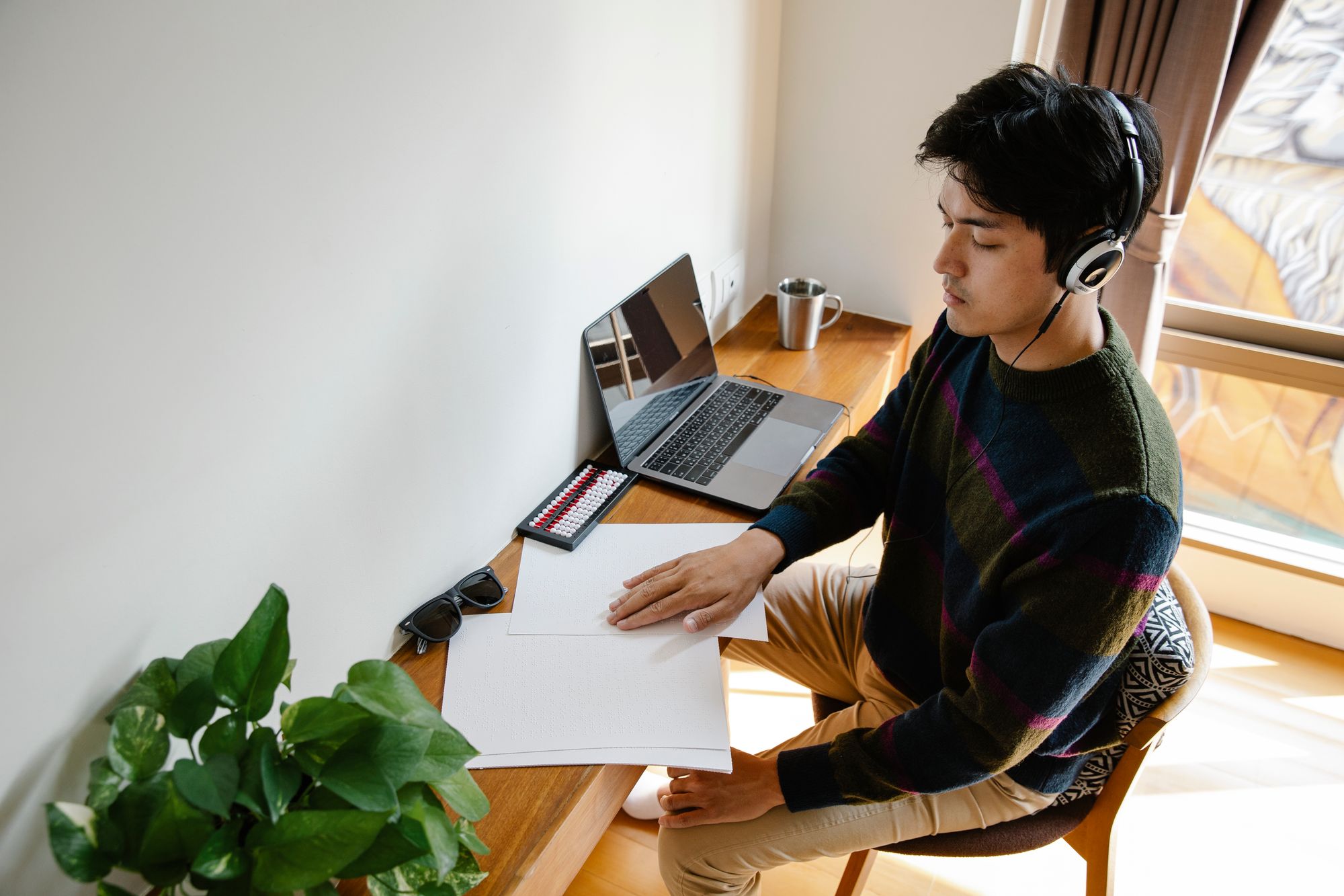 A person wearing headphones at a clear desk with one laptop, focused on a page.