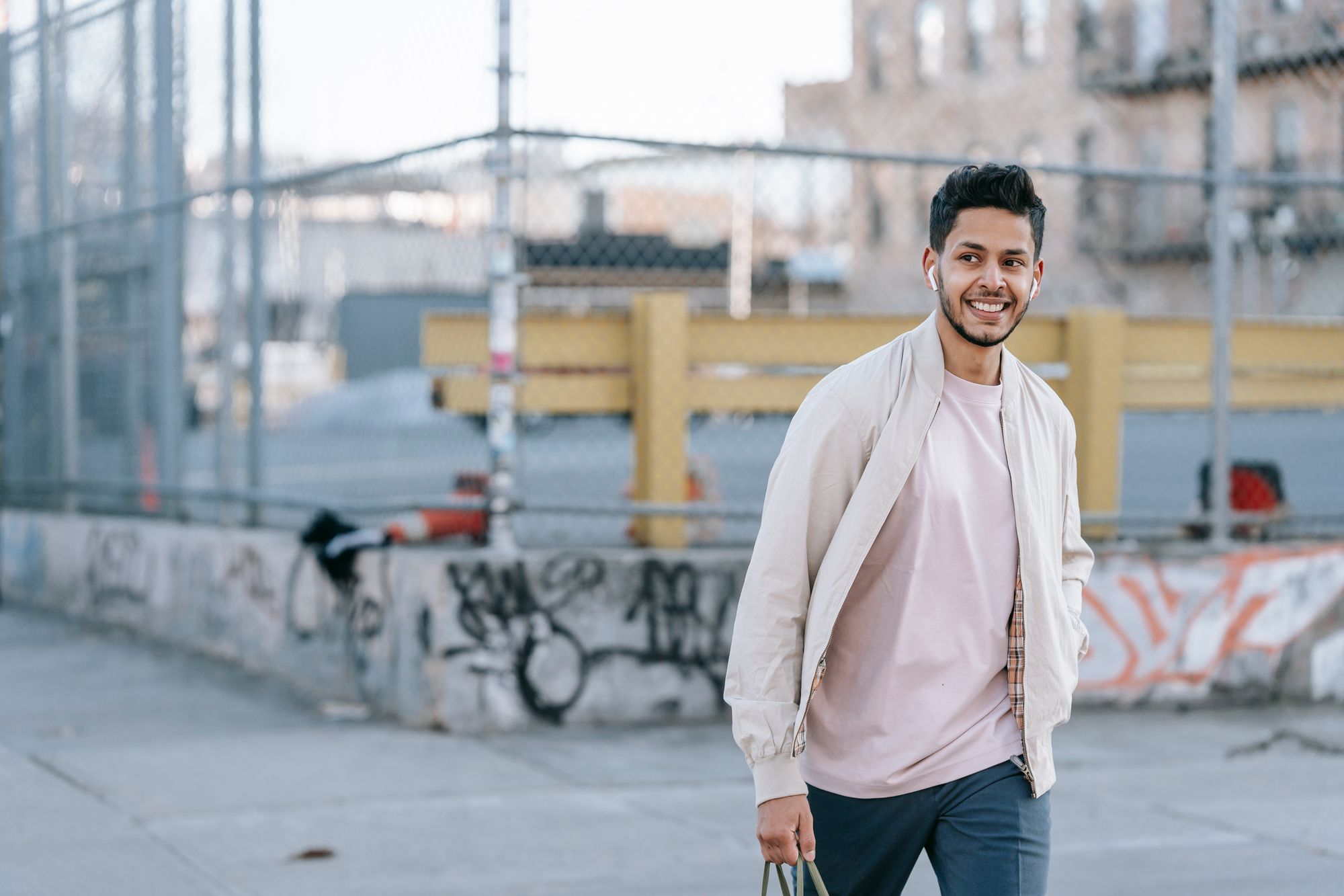 A person walking down a city street with earbuds in, talking and smiling.