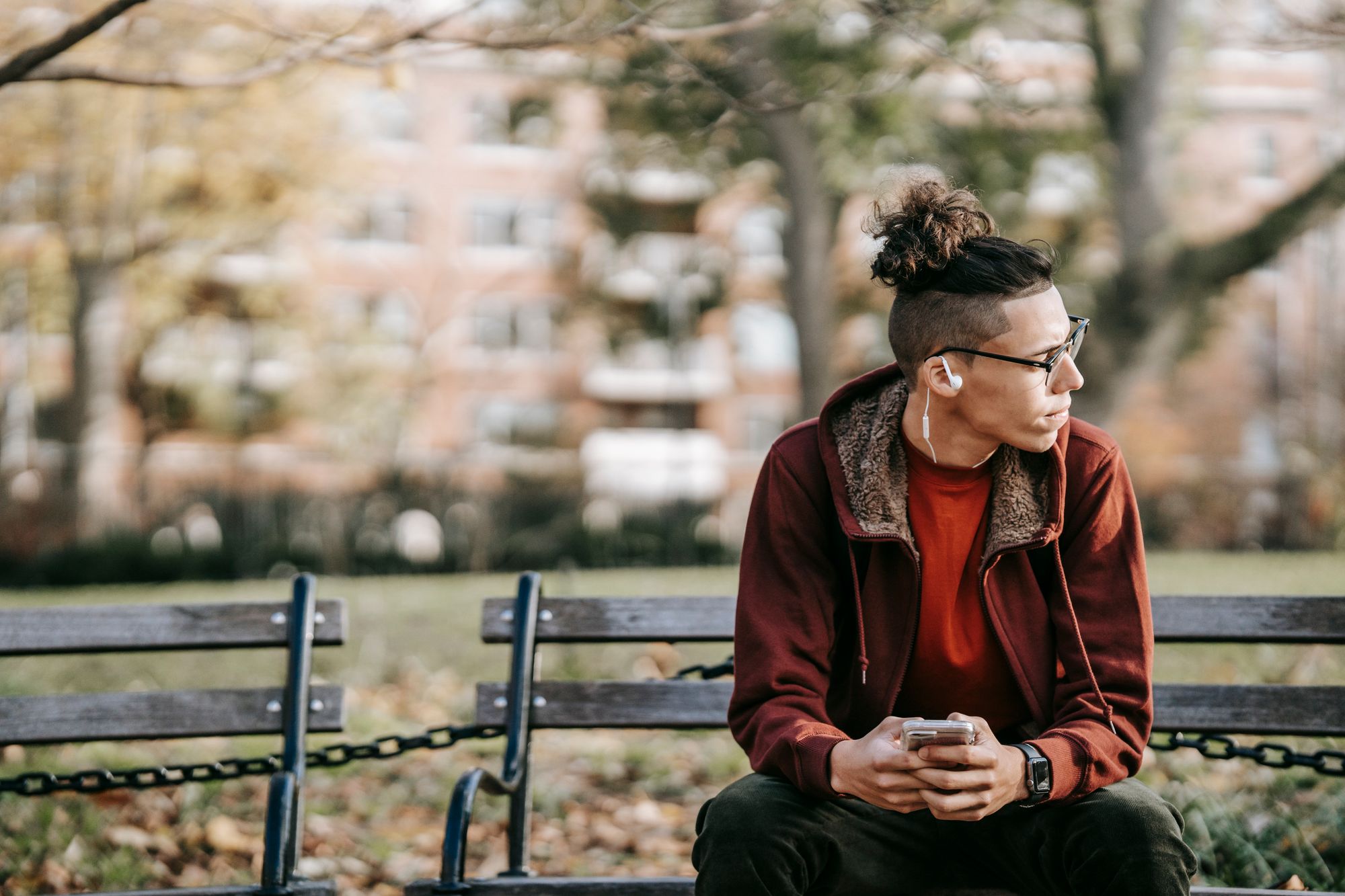 A person on a park bench holding a phone, looking away before typing.