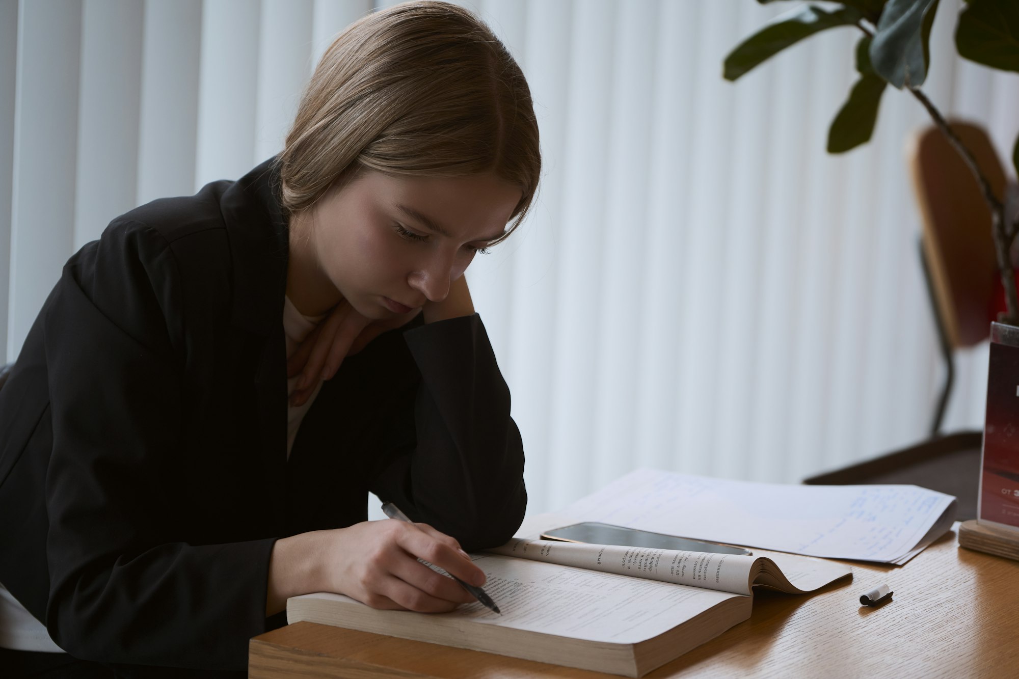A person at a desk with one open book, making notes.